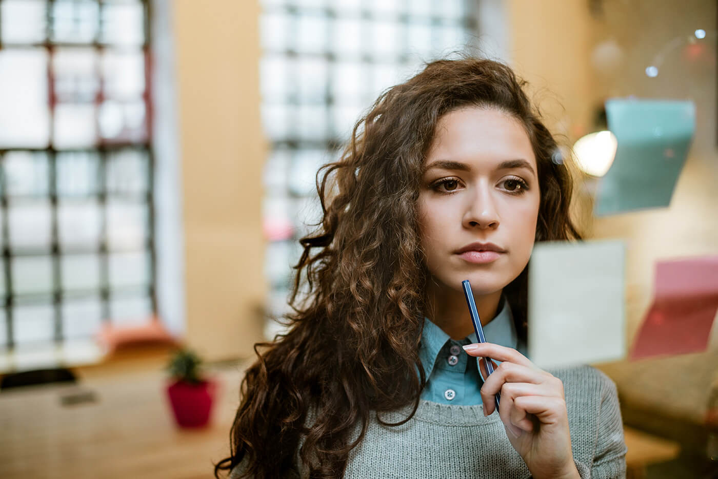 A young woman thinking through a plan or thought process with post it notes on a glass planning board